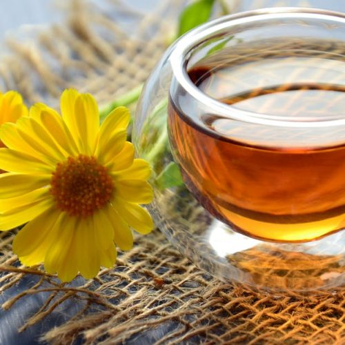 Glass cup of herbal tea with yellow flowers on a textured background.