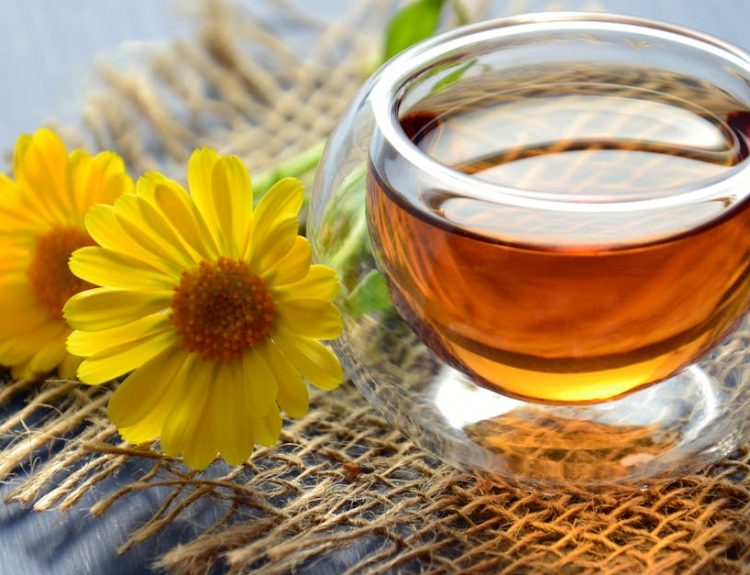 Glass cup of herbal tea with yellow flowers on a textured background.