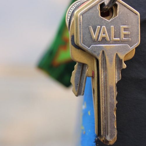 A detailed view of a metallic key with 'Vale' engraved on it, hanging against a blurred background.
