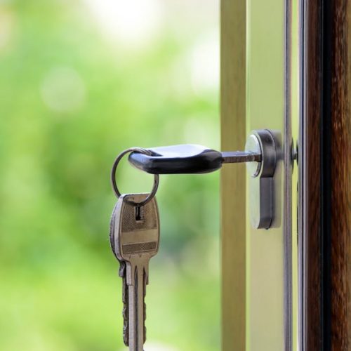 Key inserted in door lock against a blurred green background, symbolizing security and real estate.