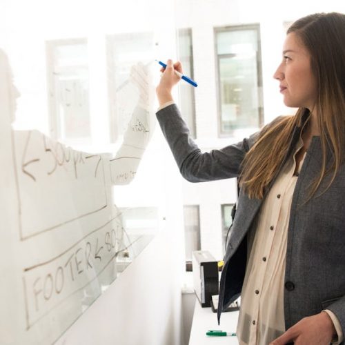 Professional woman writing on a whiteboard in an office environment, focusing on ideas.