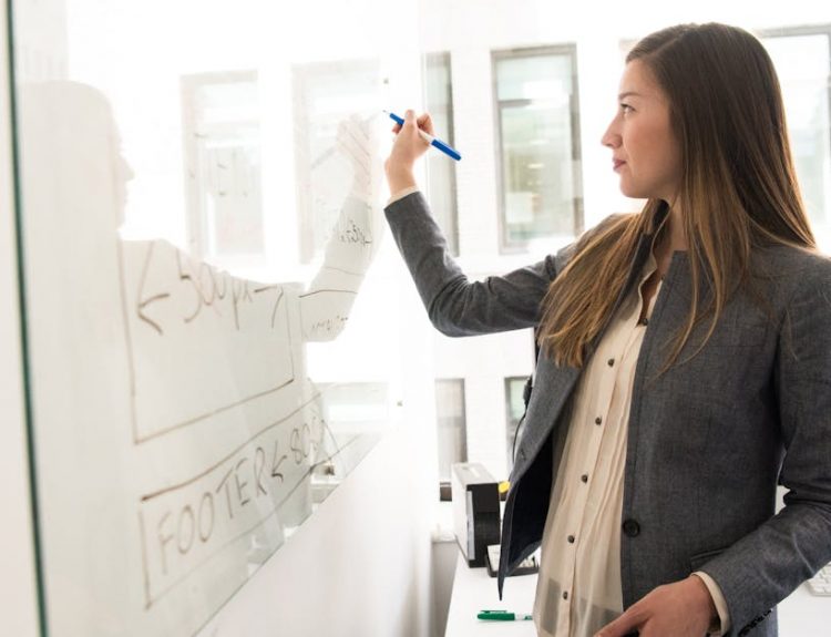 Professional woman writing on a whiteboard in an office environment, focusing on ideas.