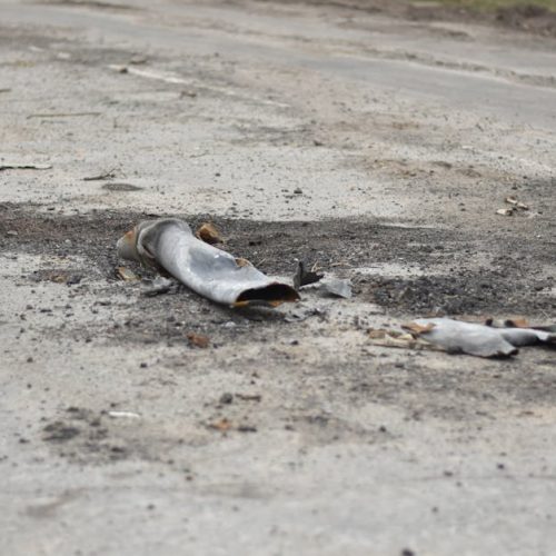A fragment of a military shell lies on a rural road, depicting destruction.
