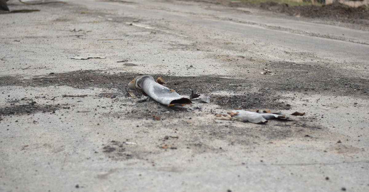 A fragment of a military shell lies on a rural road, depicting destruction.
