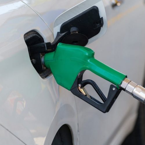 Close-up of a green nozzle refueling a white car at a gas station.