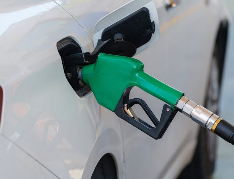 Close-up of a green nozzle refueling a white car at a gas station.