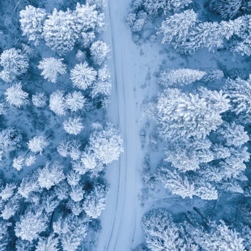 A mesmerizing aerial perspective of a snowy winter forest with a winding path.
