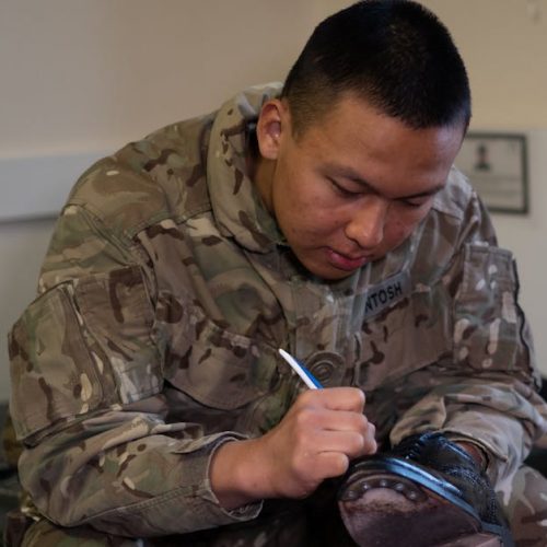 A British soldier is polishing boots indoors, showcasing military routine and discipline.