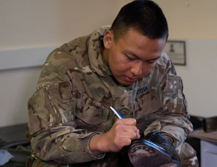 A British soldier is polishing boots indoors, showcasing military routine and discipline.