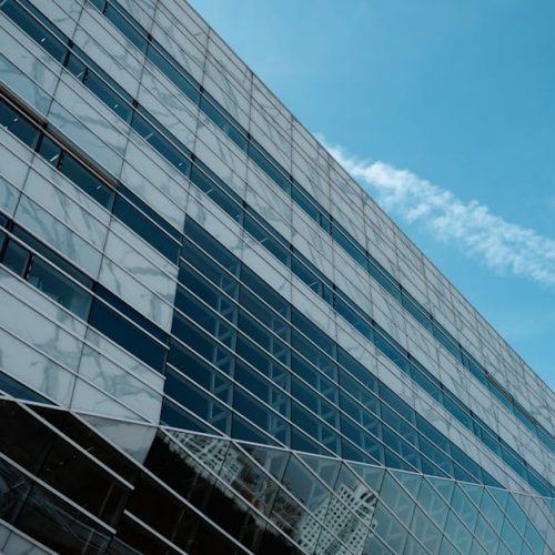 A striking low angle view of a modern glass building against a clear blue sky, emphasizing urban architecture.