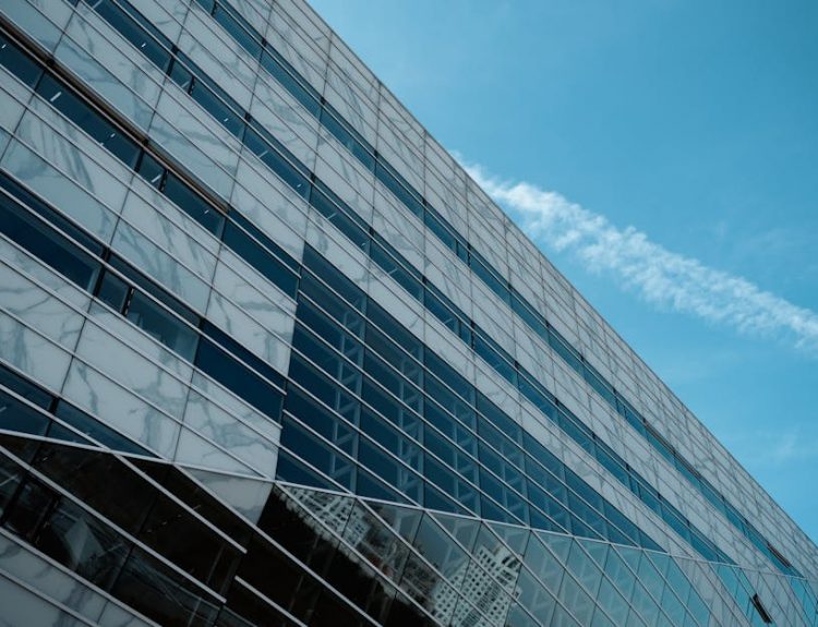 A striking low angle view of a modern glass building against a clear blue sky, emphasizing urban architecture.