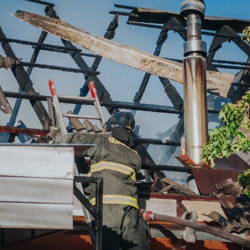 A firefighter tackles the aftermath of a house fire, clearing debris from a burned roof.