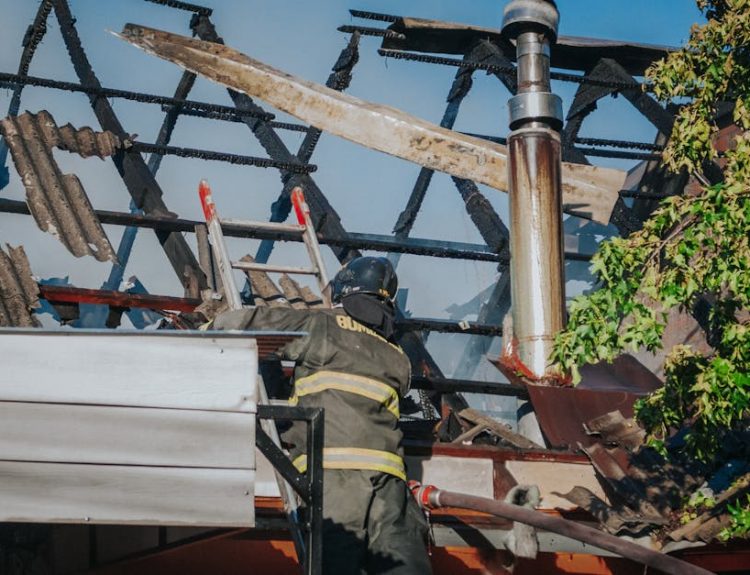 A firefighter tackles the aftermath of a house fire, clearing debris from a burned roof.