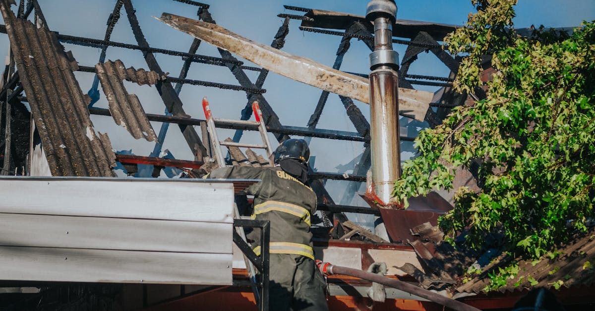 A firefighter tackles the aftermath of a house fire, clearing debris from a burned roof.
