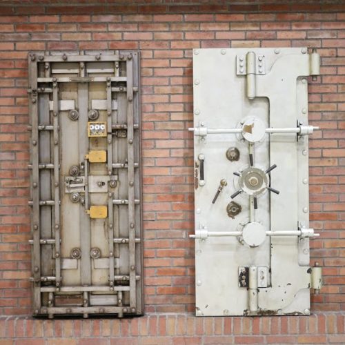 Two steel security vault doors attached to a vintage brick wall, showcasing industrial strength.