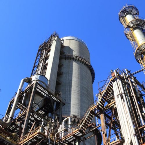 A towering industrial plant under a vivid blue sky, showcasing its intricate architecture and industrial prowess.