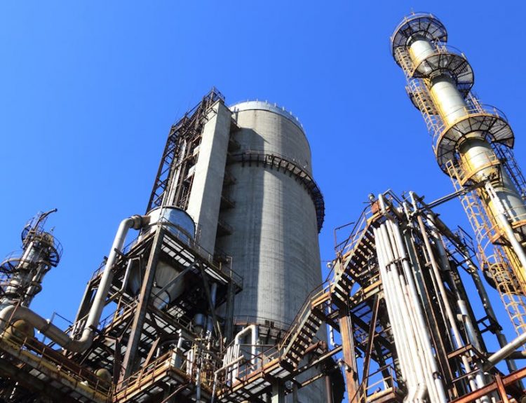 A towering industrial plant under a vivid blue sky, showcasing its intricate architecture and industrial prowess.