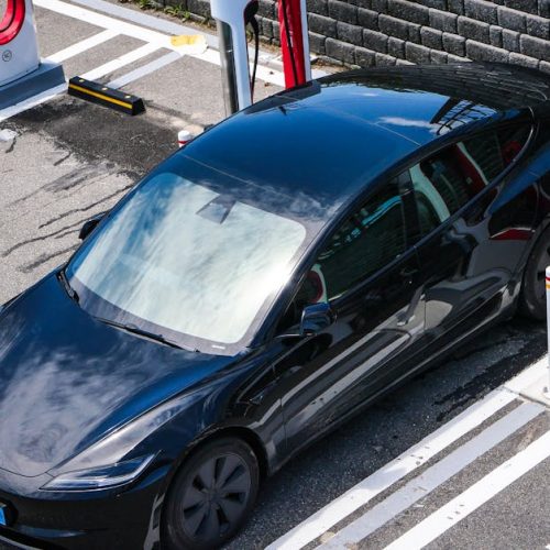 A black Tesla parked at a charging station in an urban setting.