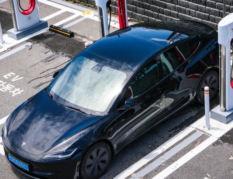 A black Tesla parked at a charging station in an urban setting.