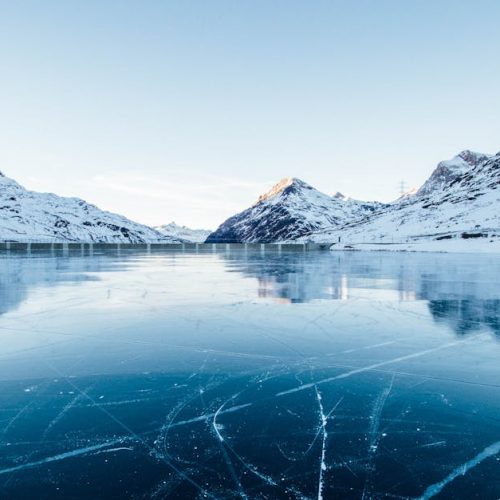 A serene winter landscape featuring a frozen lake surrounded by snow-covered mountains in Switzerland.