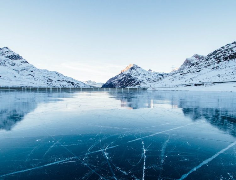 A serene winter landscape featuring a frozen lake surrounded by snow-covered mountains in Switzerland.