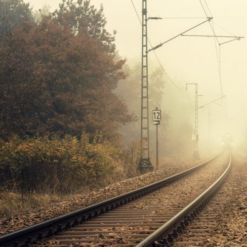Foggy autumn scene of railway tracks disappearing into mist amidst colorful trees.