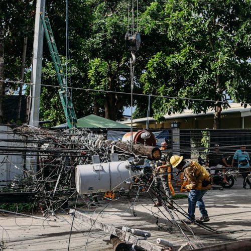 Team of workers in hard hats repairing electrical lines from a fallen pole after an accident.