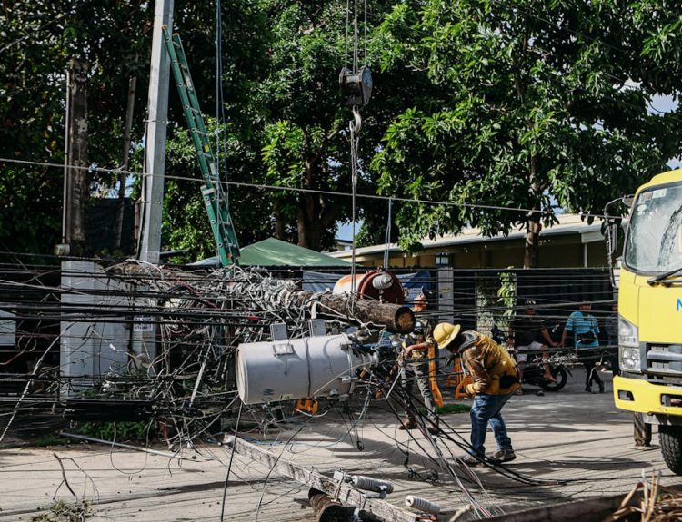 Team of workers in hard hats repairing electrical lines from a fallen pole after an accident.