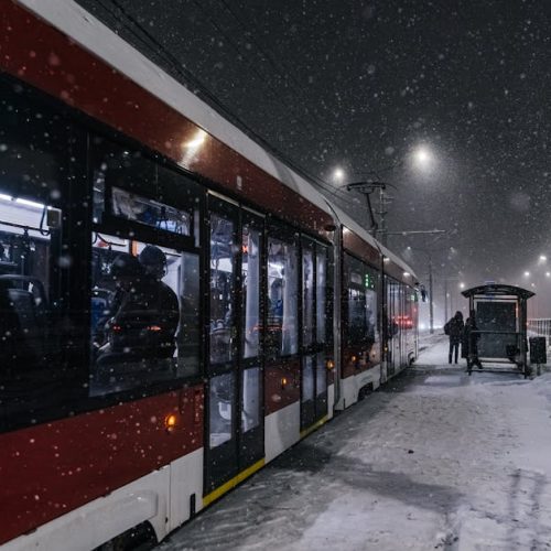 A red tram at a snowy stop on a winter's night, capturing urban life.