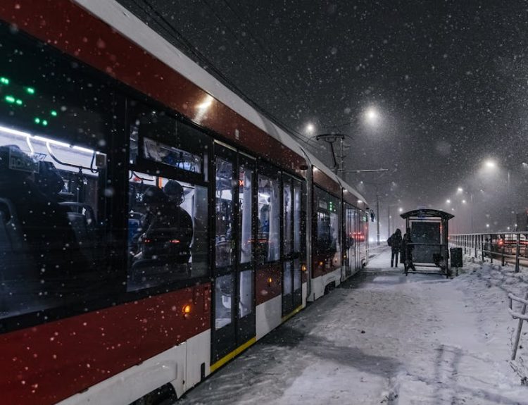 A red tram at a snowy stop on a winter's night, capturing urban life.