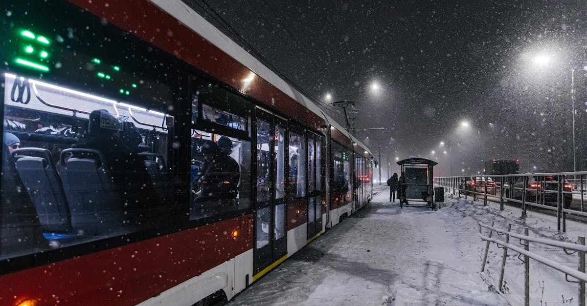 A red tram at a snowy stop on a winter's night, capturing urban life.