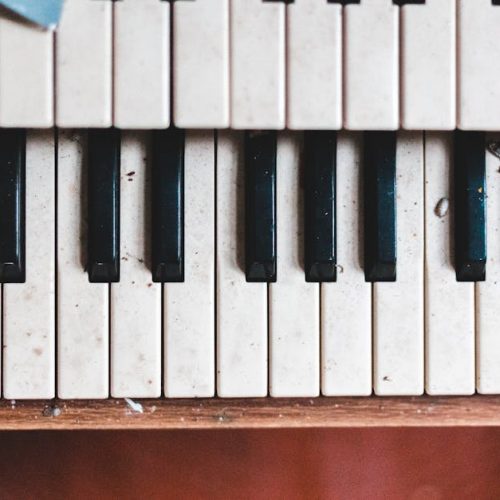 A detailed view of dusty, partially broken piano keys in an abandoned indoor setting, depicting decay.