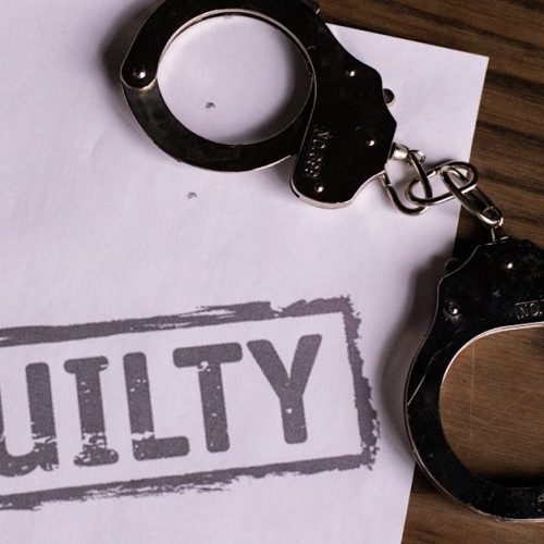 Top view of handcuffs on paper with 'GUILTY' text, symbolizing a verdict or crime.