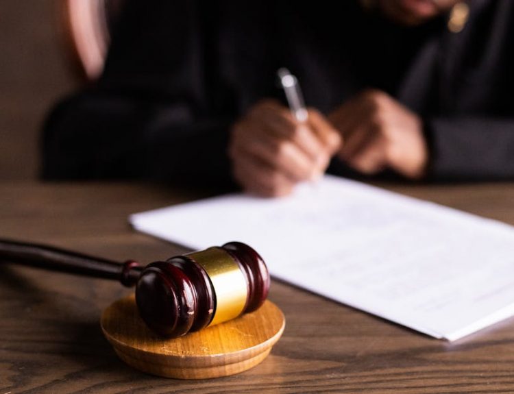 Judge signing documents at desk with focus on gavel, representing law and justice.