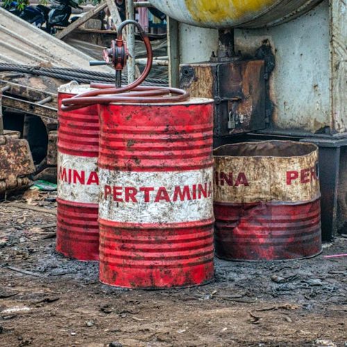 Rusted Pertamina oil barrels in an industrial waste area outdoors in Jakarta, Indonesia.