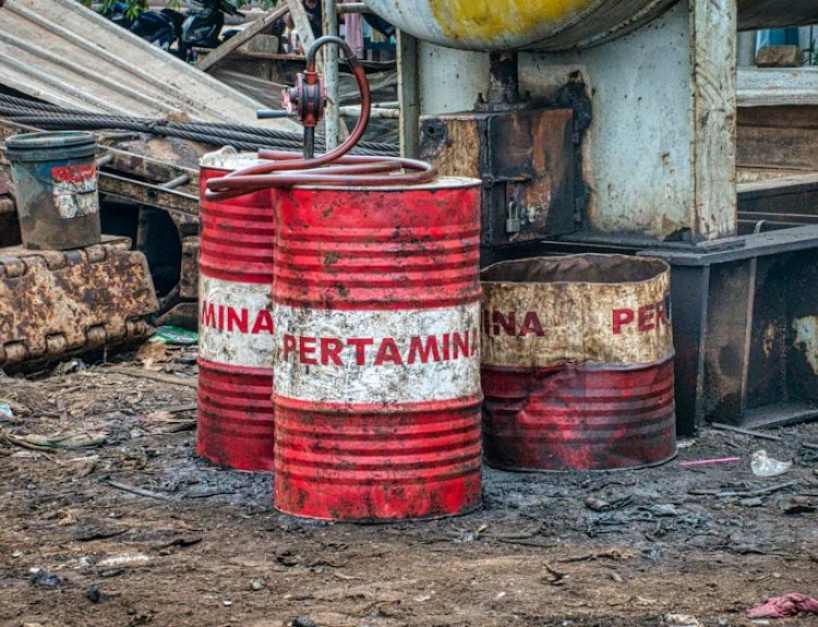Rusted Pertamina oil barrels in an industrial waste area outdoors in Jakarta, Indonesia.