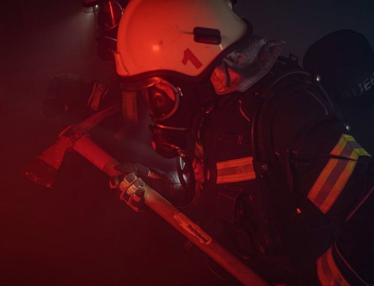 Firefighters in full gear with helmets and axes tackle a smoky emergency situation.
