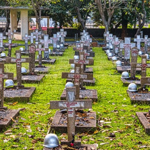 A serene view of a military cemetery in Jakarta featuring cross headstones and lush greenery.