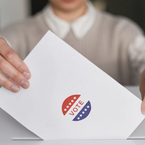 A person casting a vote by placing a ballot into a ballot box, symbolizing democratic participation.