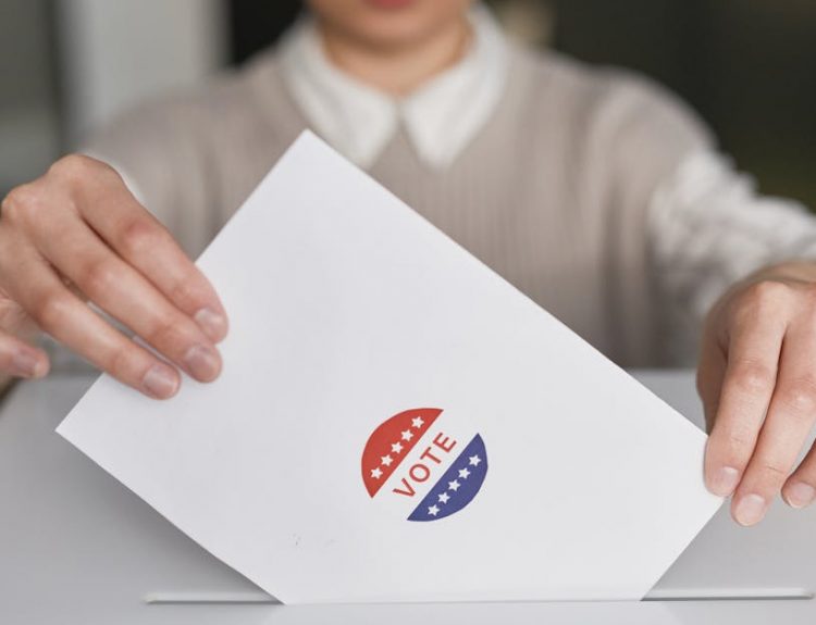 A person casting a vote by placing a ballot into a ballot box, symbolizing democratic participation.