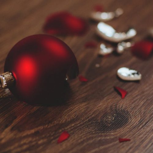 A close-up image of a broken red Christmas ornament on a wooden floor.