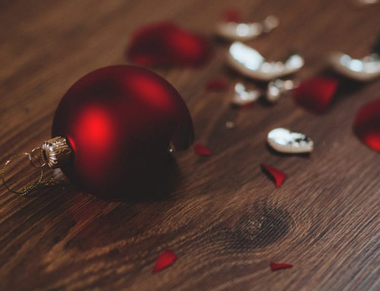 A close-up image of a broken red Christmas ornament on a wooden floor.