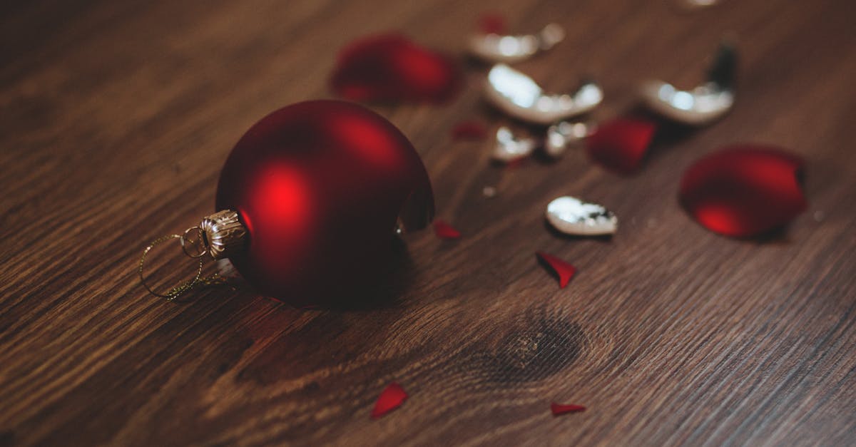 A close-up image of a broken red Christmas ornament on a wooden floor.