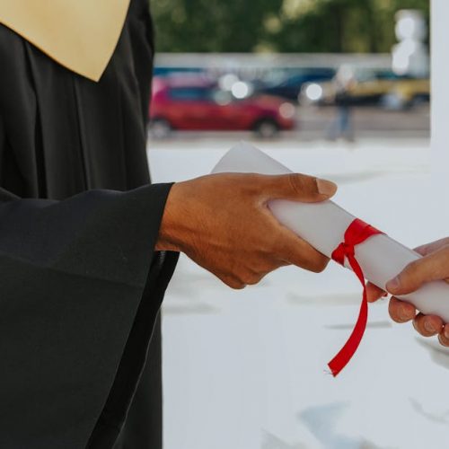 Close-up of a graduate receiving a diploma outdoors in cap and gown.