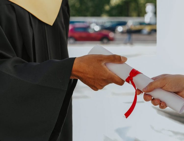 Close-up of a graduate receiving a diploma outdoors in cap and gown.