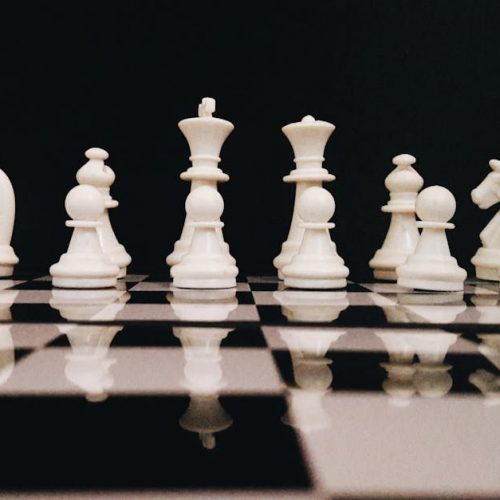White chess pieces strategically placed on a board reflecting against a black background.