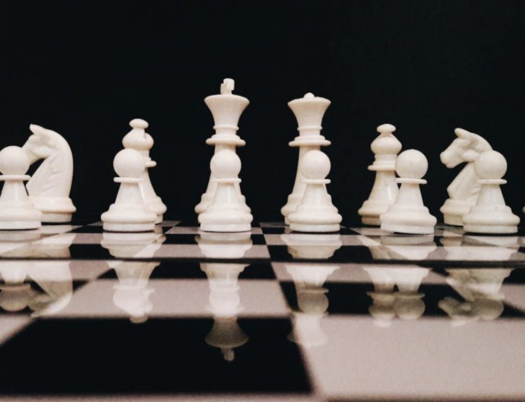 White chess pieces strategically placed on a board reflecting against a black background.
