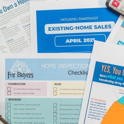 Flat lay of real estate brochures, checklists, and a calculator for home buying.