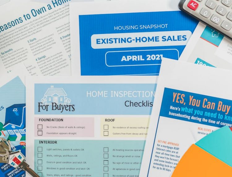 Flat lay of real estate brochures, checklists, and a calculator for home buying.