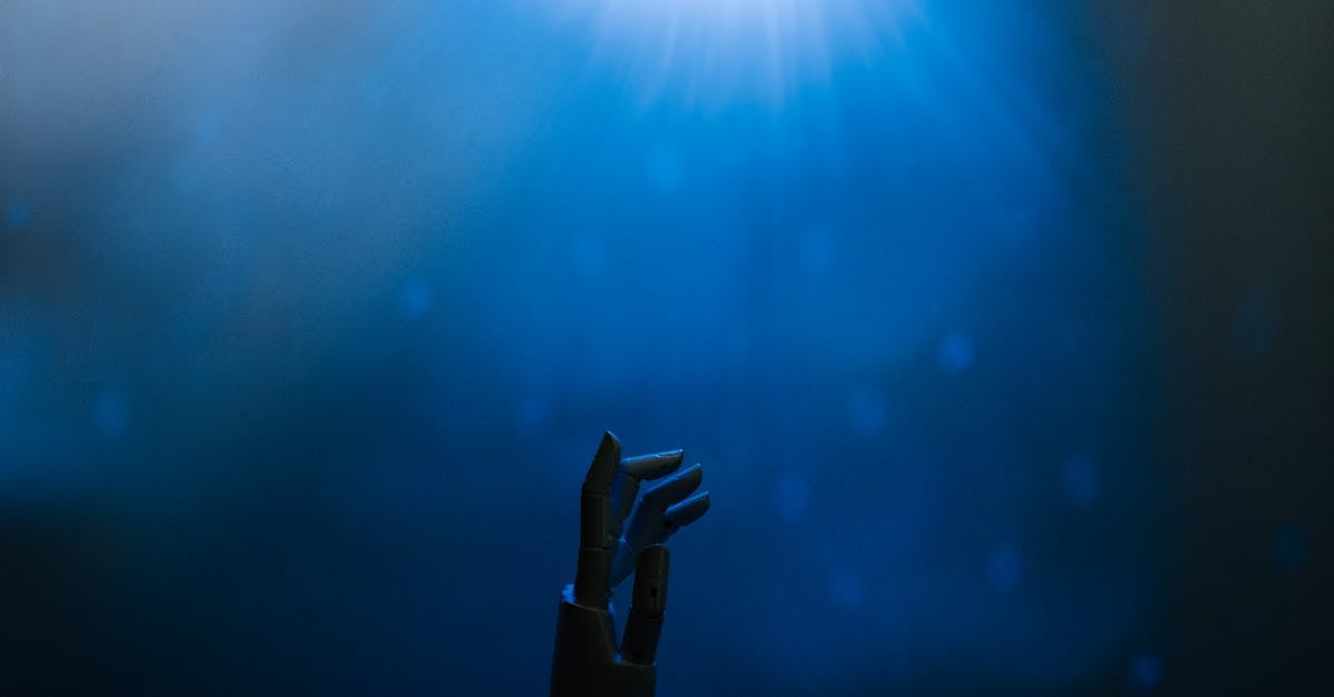 Silhouette of a robotic hand reaching towards glowing blue light in a futuristic setting.